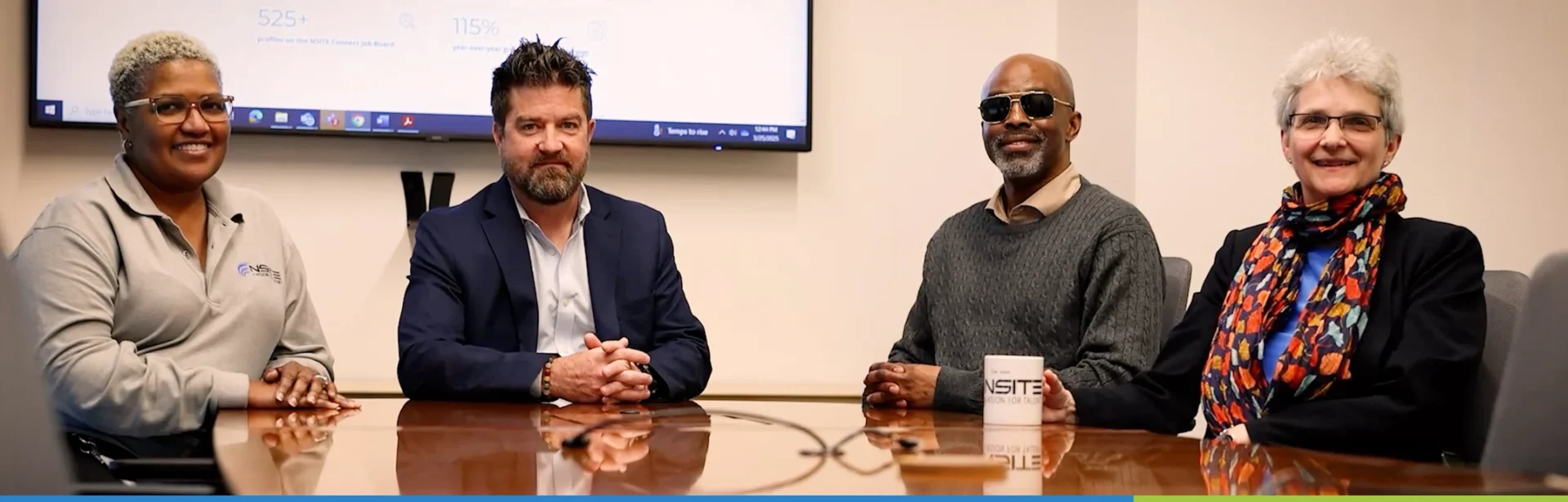 Image of NSITE team smiling and sitting at a meeting room table together.